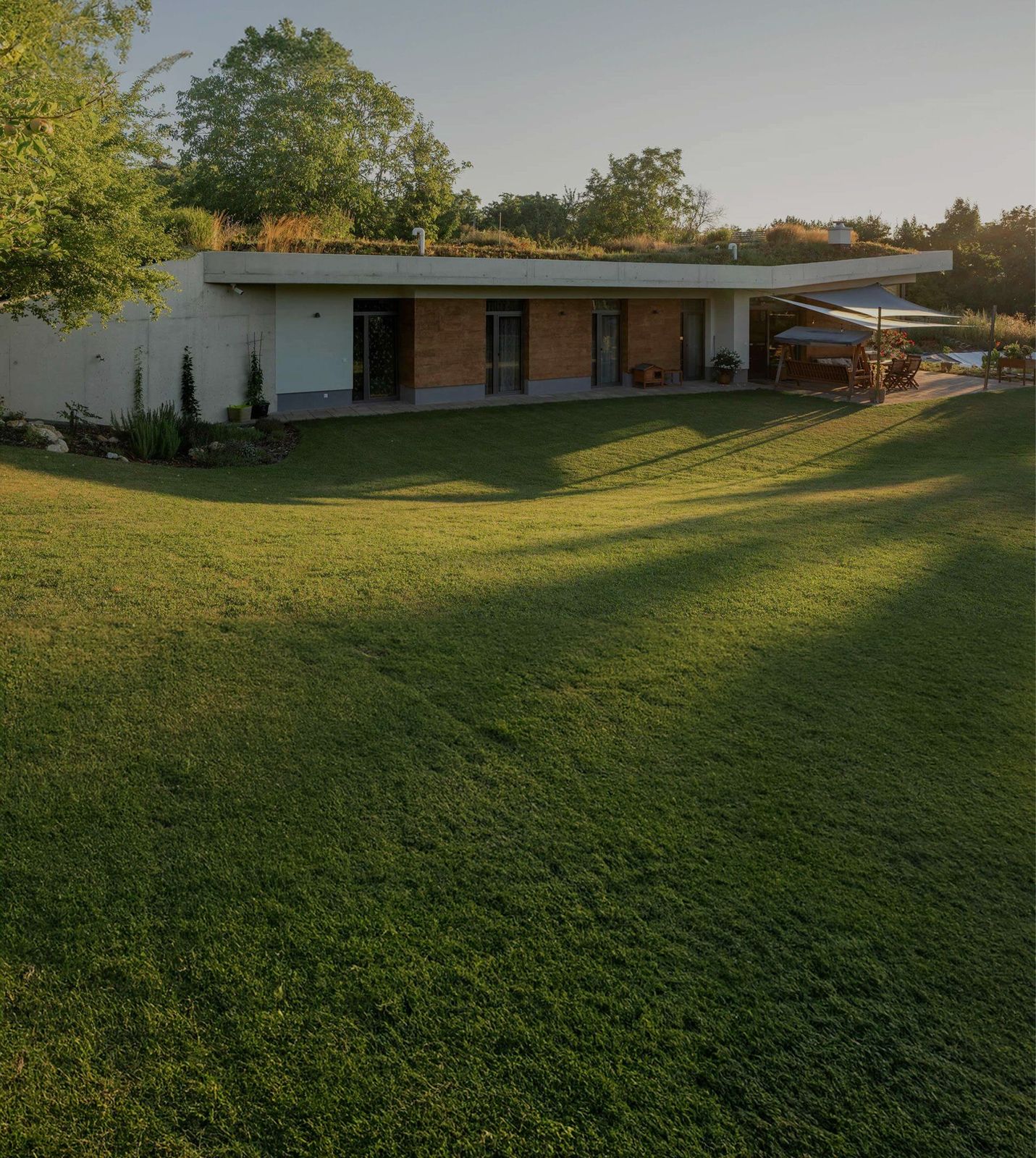 A Talpa House: a long, low front of glass and brick under a grass roof, with a lawn in front